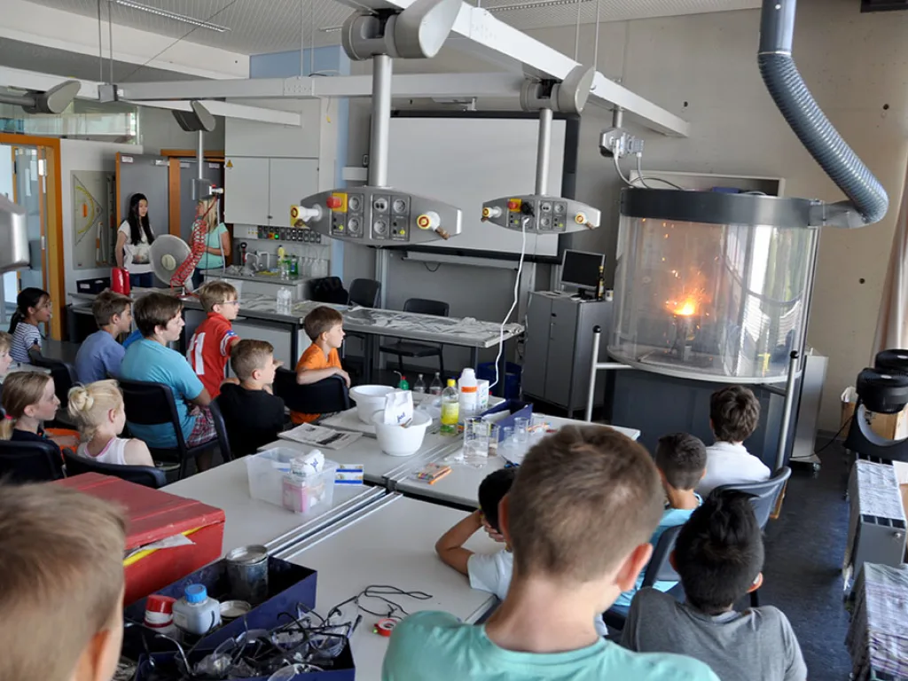 Kinder sitzen im Chemieraum und verfolgen einen Versuch am Abzug.